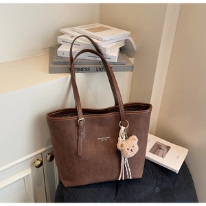 Detail of dark brown suede tote bag with brand logo and cute plush bear charm