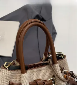 Detailed close-up of brown leather handles and beige woven body with gold hardware buckles