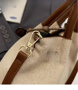 Detail of golden metal hooks on canvas and brown leather bucket bag with retro stitching