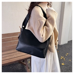 Detail of a large black oil wax leather tote bag with pleated shoulder strap and flap closure
