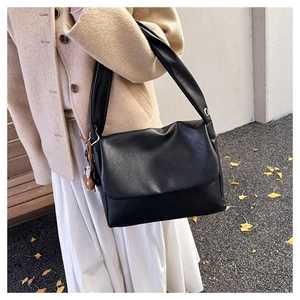 Chic black oil wax leather tote bag with bear charm shown in an autumn street setting