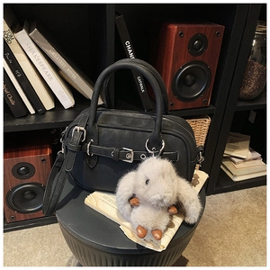 Detail of black textured boston bag with metal buckle strap and plush bunny charm