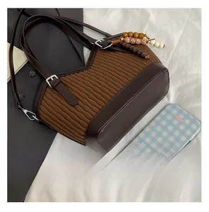 Détail de la texture plissée et du charme en perles de bois sur le sac seau marron