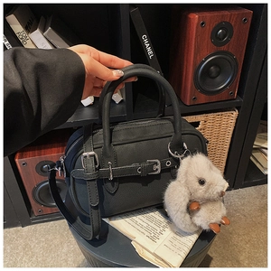 Macro detail of black litchi grain bowling bag with plush rabbit charm and metal buckle