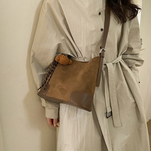 Brown matte suede bucket bag with leather trim and plush bear charm worn by a model