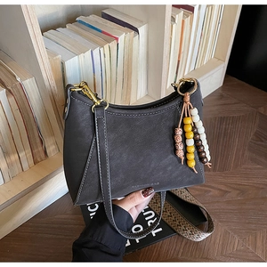 Detalle de bolso de hombro gris oscuro con costuras blancas y colgante de cuentas