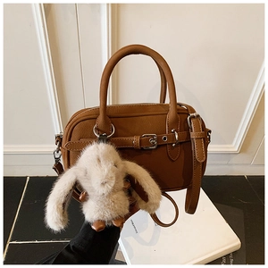 Detail of brown faux leather handbag featuring a white plush bunny charm and strap