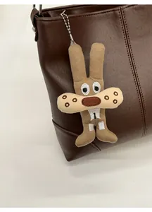 Close-up of a cartoon plush rabbit charm with metal chain on a brown leather tote bag