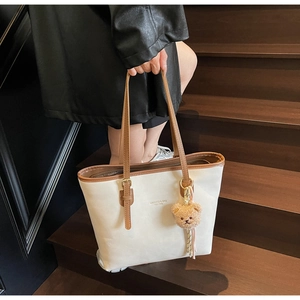 Close-up of beige faux leather tote bag with brown straps and cute teddy bear charm