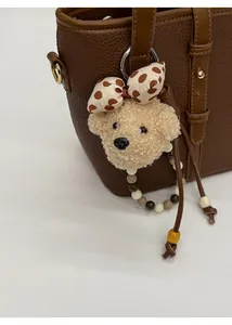 Detail of plush bear bag charm with polka dot bow and colorful beads on leather handbag