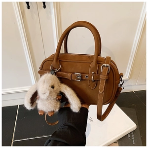 Detail of caramel brown bowling handbag featuring metal buckles and a cute plush bunny charm