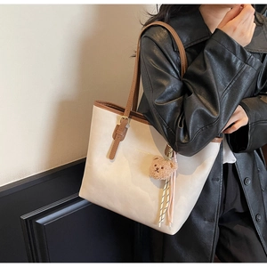 Detail of cream leather tote bag with brown straps and a plush bear charm on a model