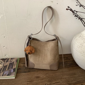 Detail of matte khaki bucket bag on wooden table with a cute brown teddy dog pendant