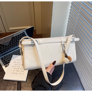 Detail of a beige crossbody bag with tri-color pompom charm on an office desk