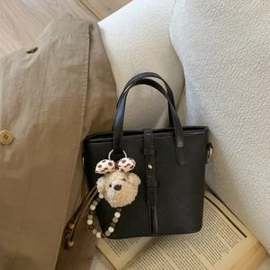 Detail of black pebbled leather bucket bag with cute teddy bear charm on sofa