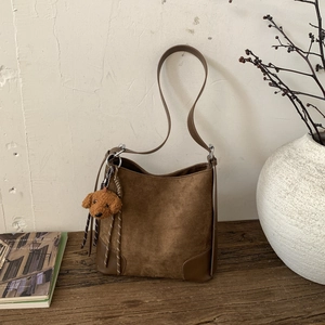 Detail of a brown matte suede hobo bag with a plush puppy charm on a wooden surface