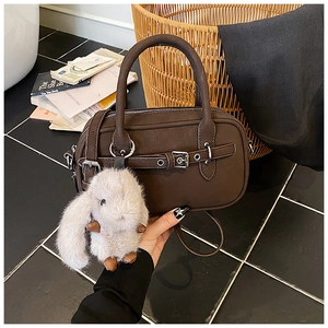 Detail of vintage brown crossbody bag with decorative buckle and white plush bunny charm
