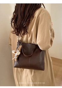 Detail of dark brown leather tote bag with vertical stitching and plush rabbit charm