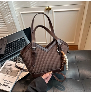 Detail der dunkelbraunen Beuteltasche mit Wellenstruktur und Perlen-Quasten-Anhänger