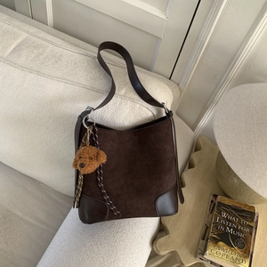 Detail of dark brown matte suede bucket bag with leather accents and plush bear charm