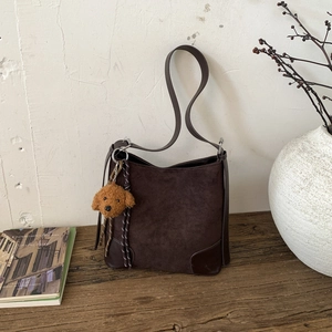 Detail of dark brown suede bucket bag with plush teddy charm on rustic wooden surface