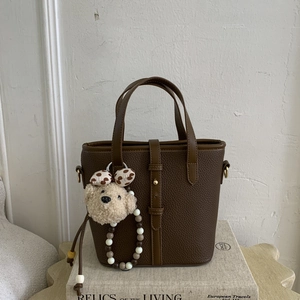 Detail of dark brown pebble leather bucket bag with plush bear charm on white background