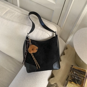 Detail of black suede bucket bag with plush bear charm and woven rope on a sofa