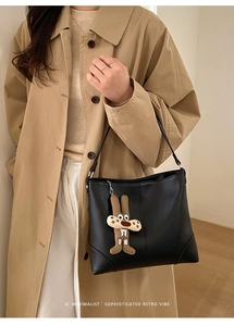 Details der schwarzen Leder-Tote-Bag mit vertikalen Nähten und süßem Kaninchen-Anhänger