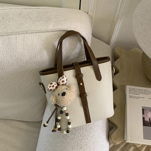 Detail of off-white lychee texture tote bag with brown straps and cute bear charm pendant