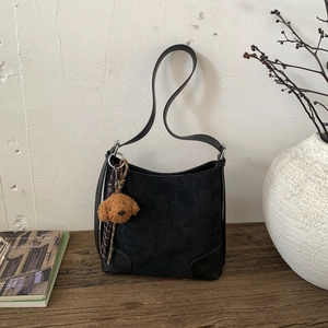 Detail of black matte suede crescent bag with cute plush puppy charm on wood surface