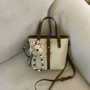 Detail view of cream pebble leather bucket bag with brown handles and plush bear charm