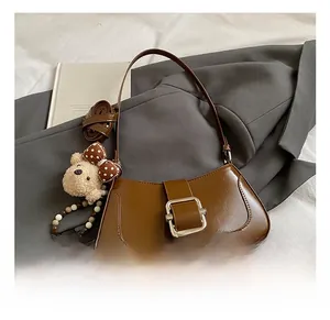 Detail showing brown leather texture, metal buckle, and bear charm on the bag