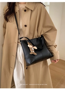 Detail of minimalist black leather tote bag featuring a cute plush bear pendant accessory
