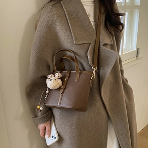 Close-up of brown lychee texture bucket bag with cute plush dog charm and metal buckle