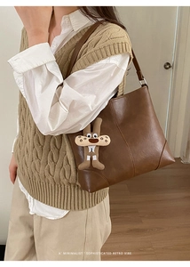 Detail of dark brown leather tote bag with a whimsical plush charm on the strap