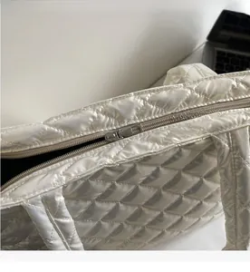 Detail of silver smooth metal zipper closure on white quilted puffer tote bag