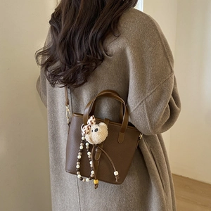 Brown lychee leather bucket bag with cute bear charm and adjustable strap on a model