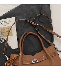 Détail du sac à main en toile et cuir marron avec son fermoir tournant en métal et sa bandoulière