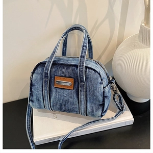 Detail of blue washed denim handbag with leather brand plate and slim shoulder strap