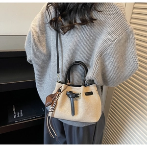 Mini beige woven bucket bag with black leather handle and heart charm on a grey sweater