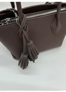 Macro view of dark brown litchi grain leather texture and dual tassel charm detail