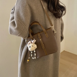 Detailed back view of a brown pebbled leather bucket bag with a plush dog charm accessory