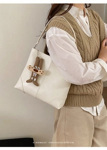 Detail of white leather tote bag featuring a cute brown character pendant and stitching