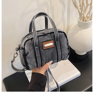 Detailed view of washed denim boston bag with brown leather patch on white books