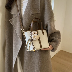 Detail of white lychee textured crossbody bag with brown leather trim and bear charm