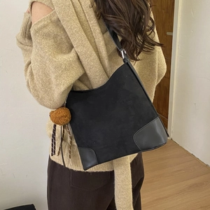Detail of black matte suede bucket bag with leather edges and plush pompom pendant