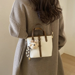 Detail view of cream bucket bag with brown trim and cute plush puppy charm on wool coat
