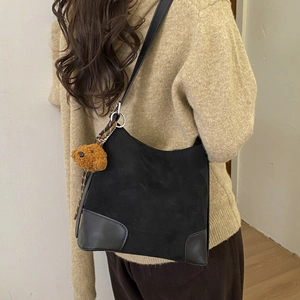 Black matte suede bucket bag shown on shoulder with a cute brown plush bear pendant charm