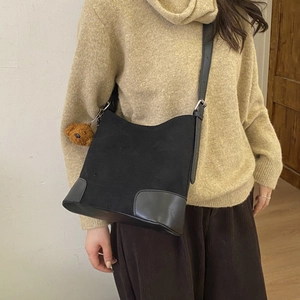 Side view of a vintage black matte bucket bag with adjustable strap and bear pendant