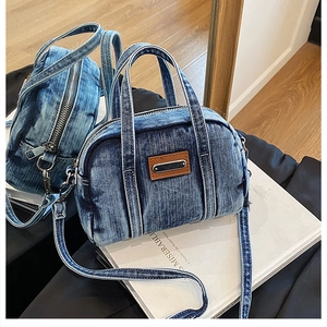 Close-up of vintage blue denim handbag with brown leather patch and metal zipper details